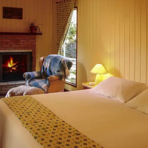 Honey-pine panelled bedroom where the bed faces a lit brick fireplace, with a plaid throw over the armchair by the window