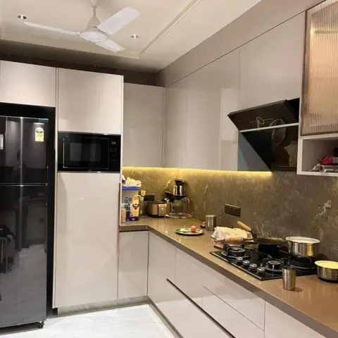 In-use L-shaped kitchen in ivory gloss handleless shutters with a gold-veined quartz counter and dado