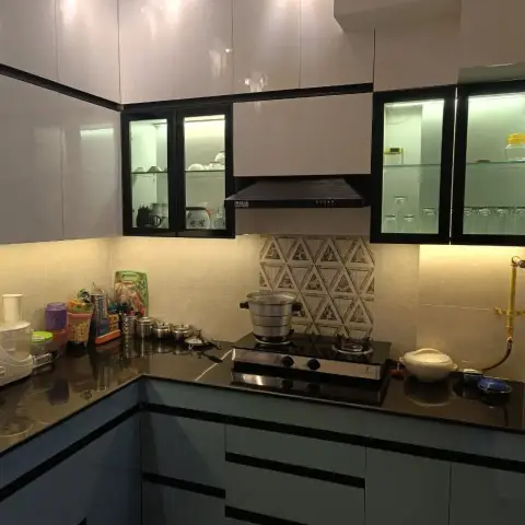 In-use L-shaped kitchen with glossy cream wall units over powder-blue base units, a black granite counter and a triangular-motif tile panel framing the hob