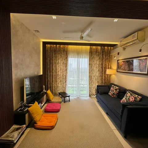 Indian living room with a dark fluted-panel TV wall, cove-lit ceiling, navy sofa with floral cushions and floor seating cushions facing a curtained balcony door