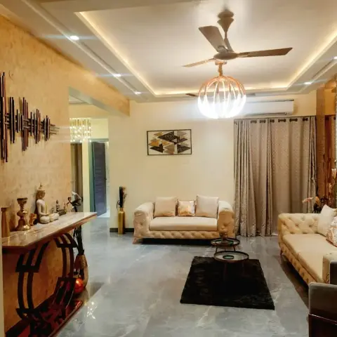 Indian living room with cove-lit stepped POP ceiling, a textured stone accent wall, tufted beige chesterfield-style sofas and a black shag rug