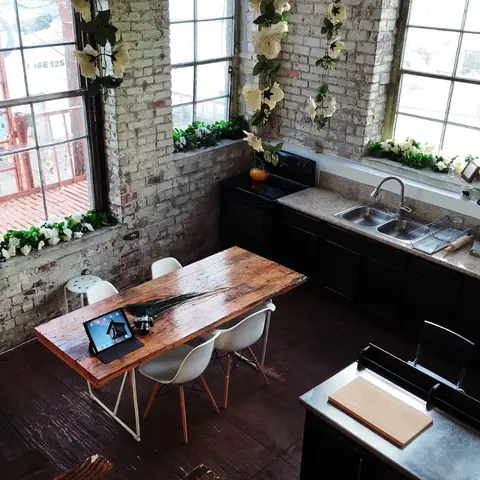 Industrial loft kitchen-dining space with exposed brick walls, tall factory windows dressed with trailing white flowers