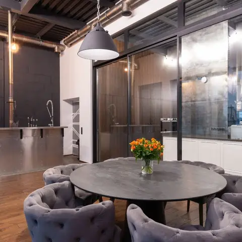 Industrial-style dining nook with a round black stone table, tufted grey velvet chairs