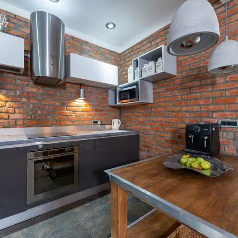Industrial-style kitchen with exposed red-brick walls, glossy dark cabinetry, a grey concrete-look countertop