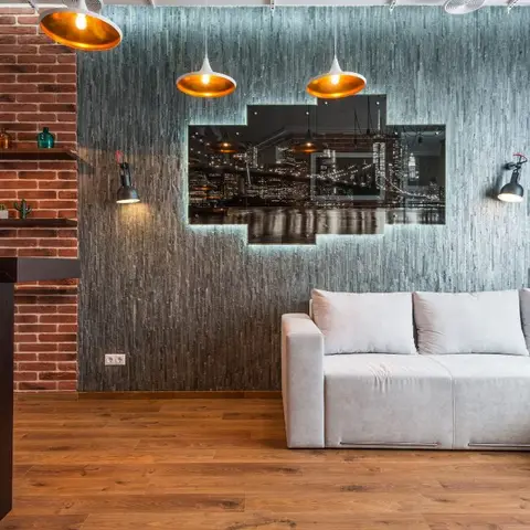 Industrial-style living room with a slate-clad accent wall framed by exposed brick, a backlit cityscape art panel, copper dome pendant lights
