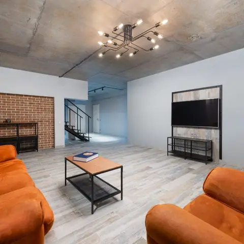 Industrial-style living room with exposed concrete ceiling, an exposed brick accent wall, and burnt-orange velvet sofas flanking a black metal coffee table.