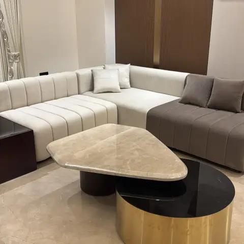 Ivory and mocha channel-tufted L-sectional against a fluted brown wood panel split by a brass reveal