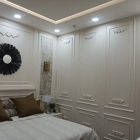 Ivory classical bedroom where ornamental appliqué motifs repeat across the wardrobe shutters and panelled walls