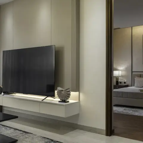 Ivory floating TV console with a concealed LED lip against a fluted plaster wall, seen past a dark veneer-framed opening into a bedroom beyond.