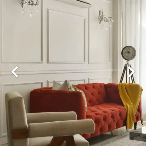 Ivory moulding-panelled living room with a rust-red button-tufted chesterfield, a mustard throw over one arm