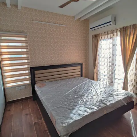 Just-handed-over bedroom with beige damask wallpaper behind a dark storage bed whose mattress is still in its plastic wrap