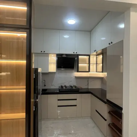 Just-handed-over kitchen in cream gloss shutters with a black granite counter and marble-look dado, backlit glass niches flanking the chimney