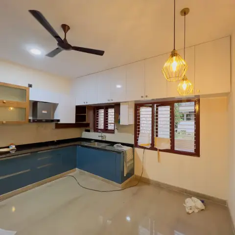 Just-installed L-shaped kitchen with teal gloss base units and white overheads, a pair of gold cage pendants hanging over the empty floor and a rosewood-framed