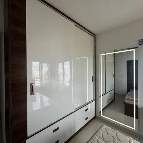 Just-installed white high-gloss sliding wardrobe with dark walnut edge bands and drawer bank