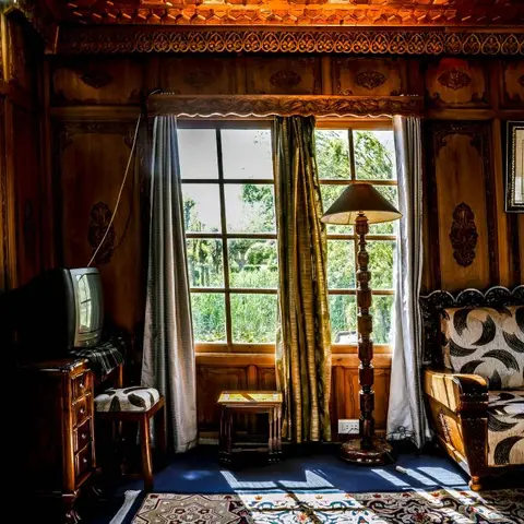 Kashmiri walnut-carved sitting room where a black-and-white crescent-print settee and a turned floor lamp face a garden window framed by striped and gold