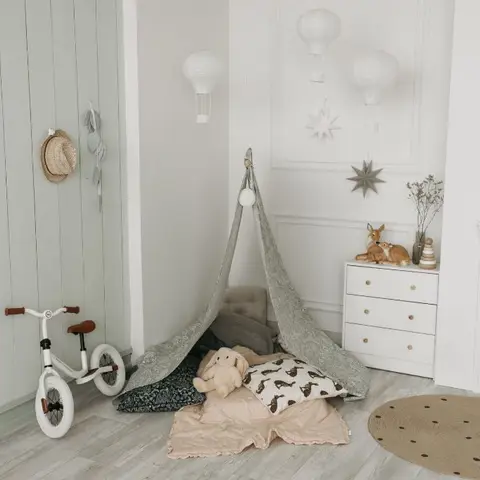 Kids' bedroom corner with a fabric reading teepee, a white three-drawer console, hanging paper balloon lanterns, and a round jute rug on a light wood floor.