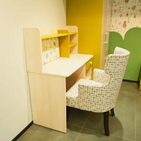 Kids' bedroom corner with a light-wood study desk, yellow accent shelving, animal-print wallpaper panel and a green cloud-shaped upholstered headboard
