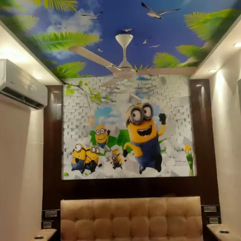 Kids' bedroom shot looking up at a Minions mural bursting through a 3D brick wall above the tufted beige headboard