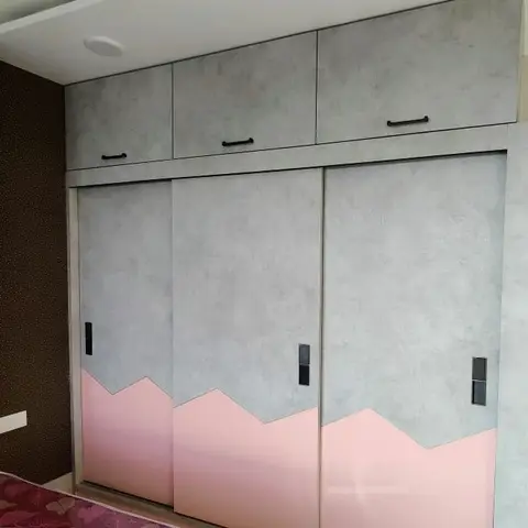 Kids' bedroom sliding wardrobe in grey with a pink mountain-motif base, beside a glimpse of a patterned bedspread.