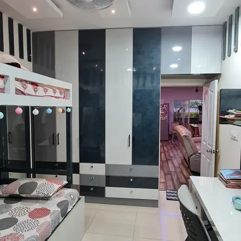 Kids' bedroom with a black-and-white glossy sliding wardrobe, a bunk bed strung with pompom lights and patterned bedding