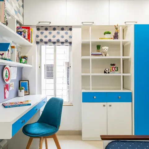 Kids' bedroom with a blue-accented study desk under the window and open display shelving stocked with toys and books