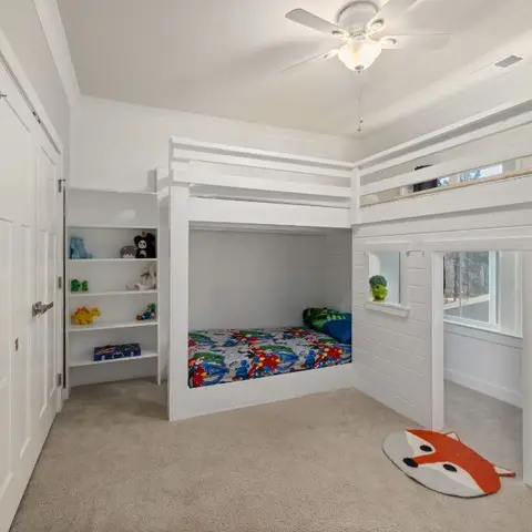 Kids' bedroom with a built-in white bunk bed nook featuring superhero bedding, a fox-shaped rug, and a bookshelf styled with picture books and toys.