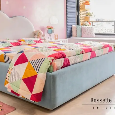 Kids' bedroom with a cloud-shaped upholstered bed in dusty blue, a rainbow patchwork quilt, a pink starred accent wall and a window seat nook.