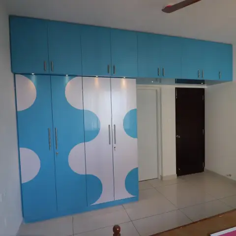Kids' bedroom with a full-height sky-blue and white wave-pattern high-gloss wardrobe spanning the wall