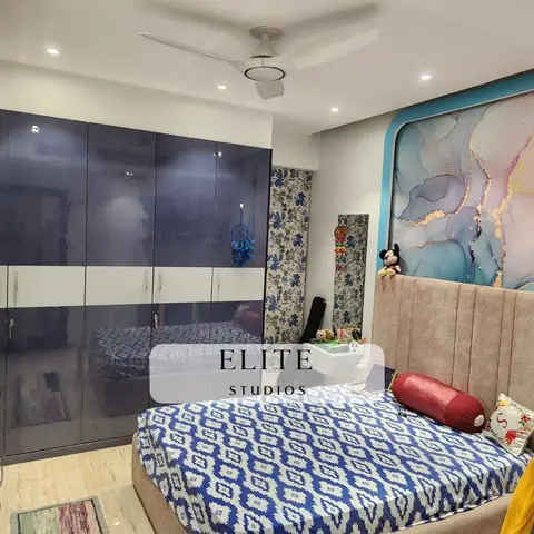 Kids' bedroom with a glossy navy-and-white wardrobe, a diamond-patterned blue bedsheet, and a channel-tufted headboard with a marbled art panel above.