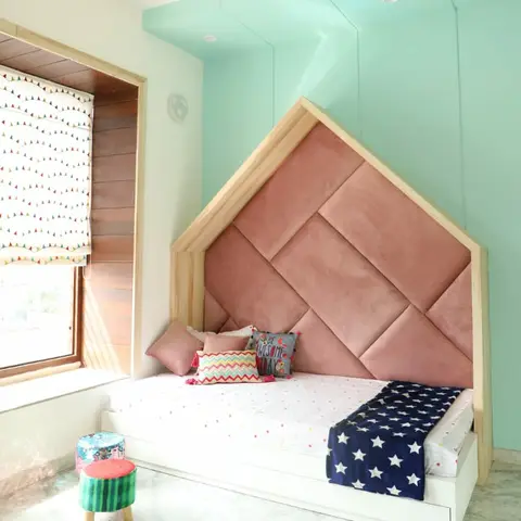 Kids' bedroom with a house-shaped upholstered blush headboard nook against a glossy mint wall, styled with a starry navy throw and colorful poufs.