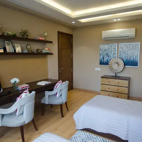 Kids' bedroom with a long built-in study desk for two seated at matching grey chairs, open wall shelving styled with books and decor
