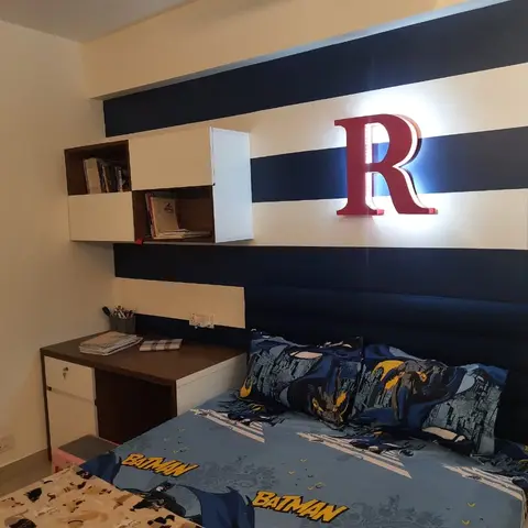 Kids' bedroom with a navy-and-white striped accent wall, a backlit monogram letter, a channel-tufted navy headboard, and Batman-themed bedding.