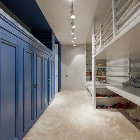 Kids' bedroom with a navy panelled wardrobe wall along one side and a white built-in bunk bed with rope-railing ladder and open toy shelving along the other.