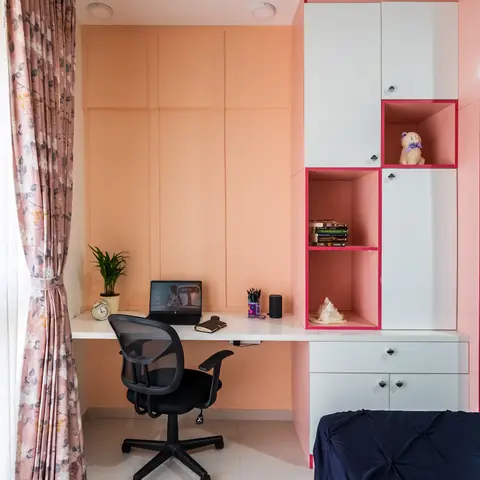 Kids' bedroom with a peach accent wall, a built-in study desk beside a white wardrobe with pink-lined open display niches holding books and a stuffed toy