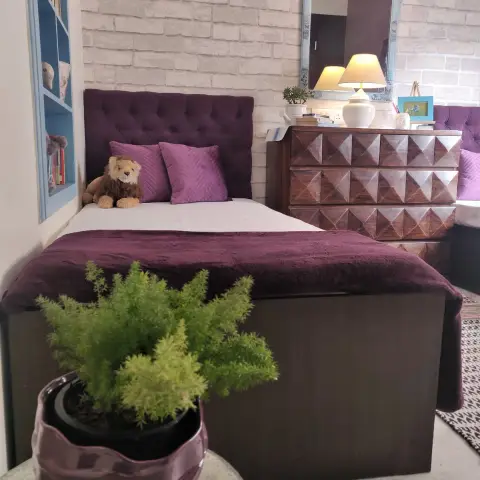 Kids' bedroom with a plum tufted upholstered bed styled with a stuffed lion toy, facing a pyramid-patterned wood dresser and an ornately framed mirror against