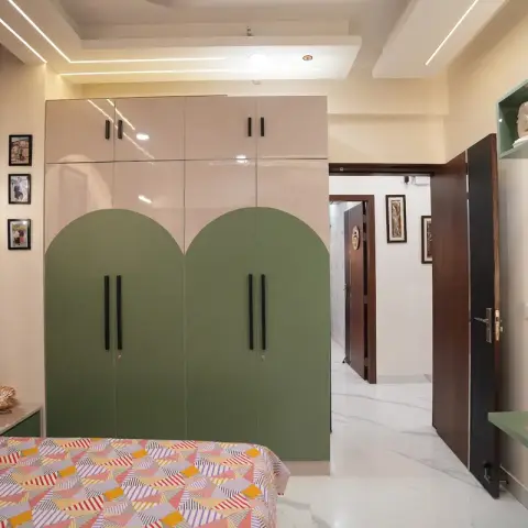 Kids' bedroom with a sage-green arch-patterned wardrobe, a wall-mounted TV on a matching green console, and a colorful geometric-print bedspread.