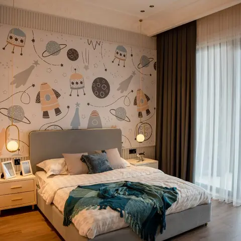 Kids bedroom with a space-and-rocket mural wallpaper behind an upholstered grey headboard, twin globe pendant lights, and a teal throw blanket on the bed.