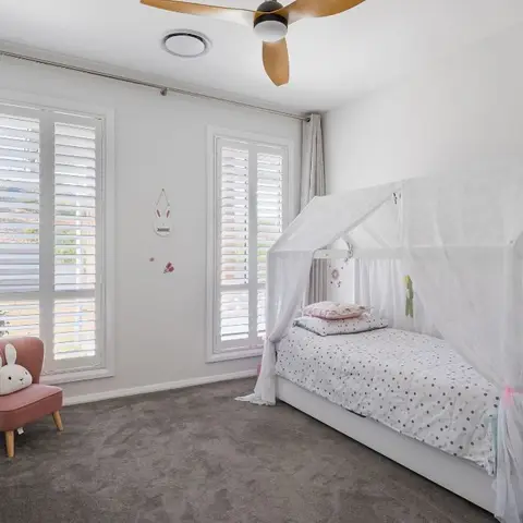 Kids bedroom with a white house-frame canopy bed dressed in polka-dot bedding, a pink stool and plantation window shutters