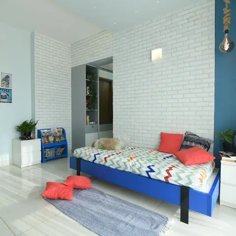 Kids' bedroom with a whitewashed brick feature wall, a blue accent wall with a rope-hung pendant light, and a blue metal-frame bed with chevron-print bedding.