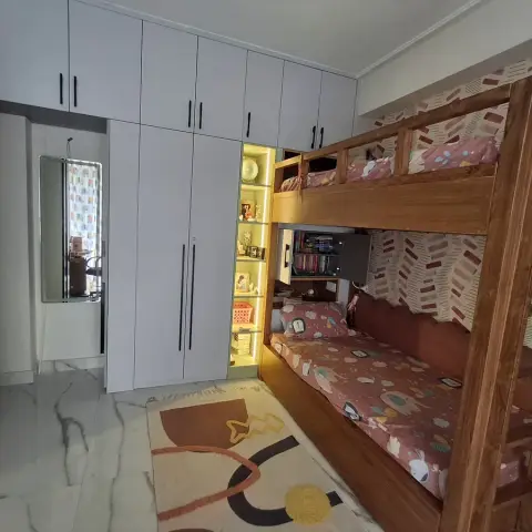 Kids' bedroom with a wood bunk bed in space-print bedding, a tall wardrobe wall, and a backlit open display shelf.