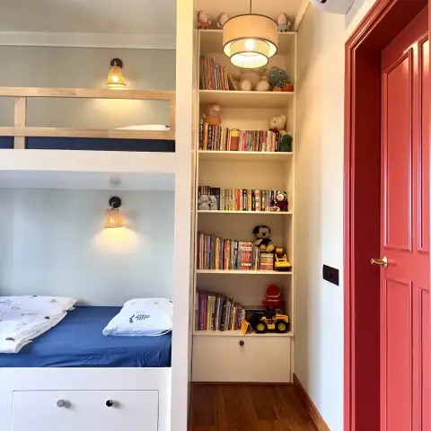 Kids' bedroom with a wood bunk bed, a built-in ladder bookshelf stacked with books and toys, and a red-painted internal door.