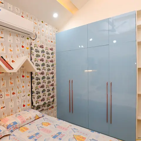 Kids' bedroom with alphabet-flashcard wallpaper, a house-shaped wall shelf, a car-print roman blind and bedsheet, and a glossy sky-blue wardrobe.