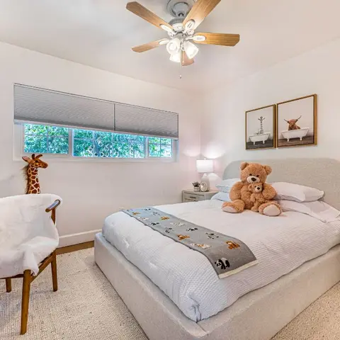 Kids bedroom with an upholstered bed dressed with an animal-print runner, teddy bears, a giraffe toy and framed animal artwork