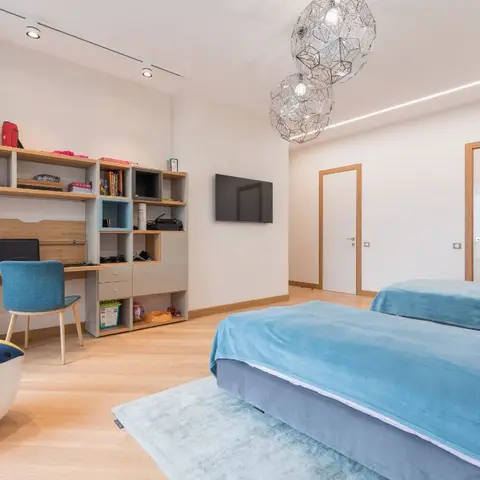Kids' bedroom with two teal velvet twin beds, a built-in study desk and open shelving stocked with toys, and faceted pendant lights