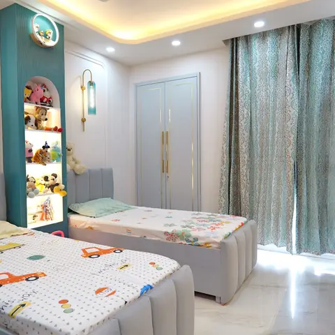 Kids' bedroom with two twin beds in car and floral print bedding, a backlit teal display alcove for stuffed toys, and a teal wardrobe with gold-trim shutters.