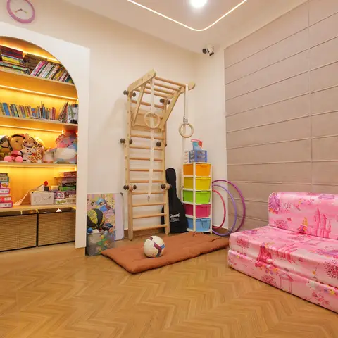 Kids' play corner with an arched backlit bookshelf, wooden climbing ladder, and a pink princess-print foldable mattress on herringbone flooring
