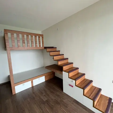 Kids room with a wood-slat loft bed built over a low daybed, integrated storage-step staircase leading up, and a small built-in desk beneath the stairs.