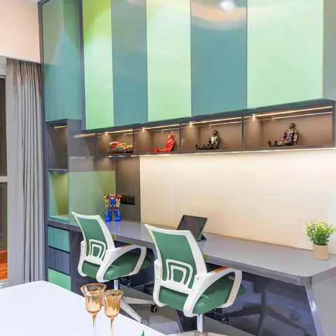 Kids' study nook with a built-in two-seater desk under green ombre high-gloss overhead cabinets and LED-lit display niches showing action figures.