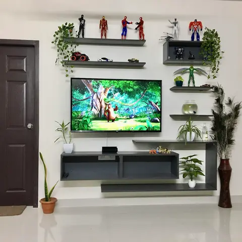 Kids-styled living room TV wall with floating grey shelves holding action figures and trailing plants around a wall-mounted television