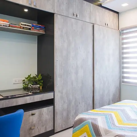 Kids/teen bedroom with a built-in study desk under open book shelving beside a concrete-textured wardrobe